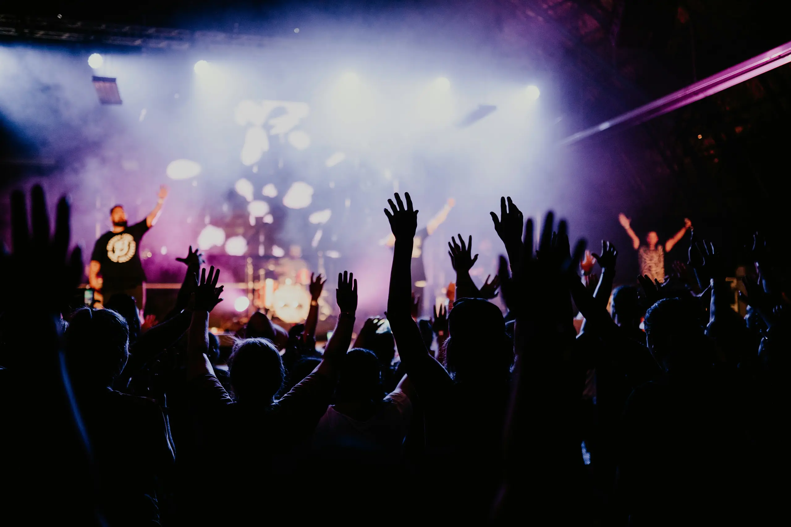 Concert crowd with hands raised under purple stage lights